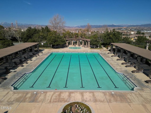 view of swimming pool with a hot tub, a mountain view, and a patio area