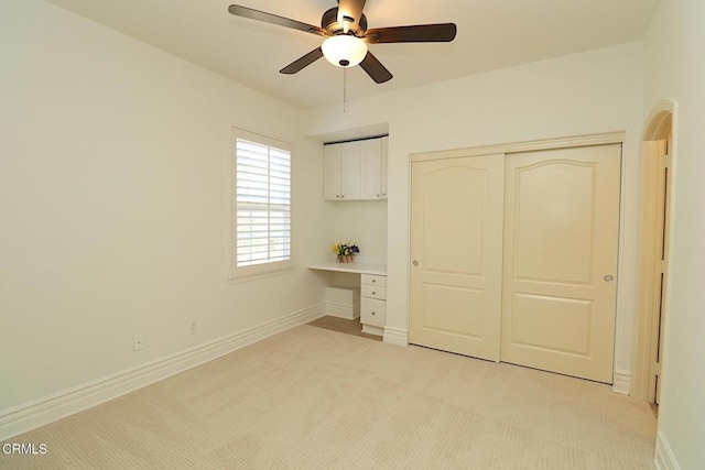 unfurnished bedroom with built in desk, light colored carpet, ceiling fan, and a closet