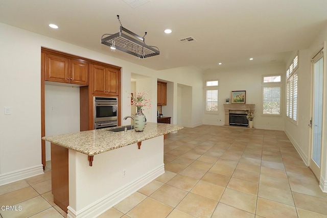 kitchen with sink, a kitchen breakfast bar, a kitchen island with sink, light tile patterned floors, and light stone counters