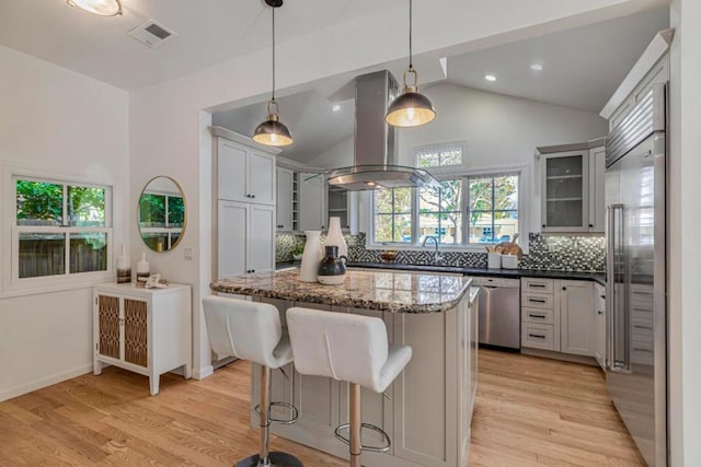 kitchen with appliances with stainless steel finishes, dark stone countertops, a center island, island exhaust hood, and decorative light fixtures