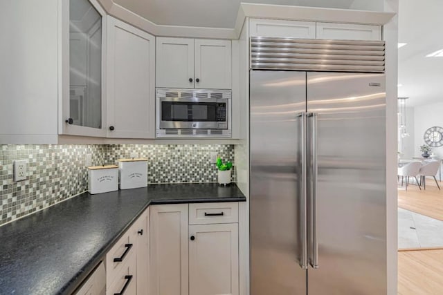 kitchen featuring built in appliances, white cabinetry, tasteful backsplash, and light wood-type flooring