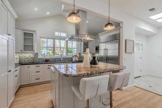 kitchen featuring built in fridge, decorative light fixtures, dark stone countertops, a kitchen bar, and light hardwood / wood-style flooring