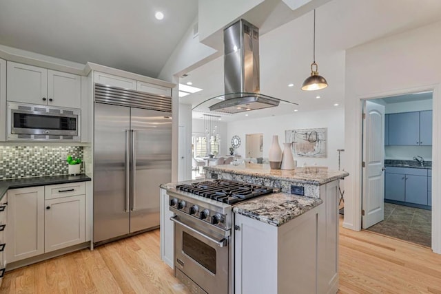 kitchen featuring white cabinets, island exhaust hood, built in appliances, and dark stone countertops