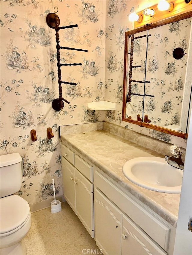 half bathroom with toilet, wallpapered walls, vanity, and baseboards