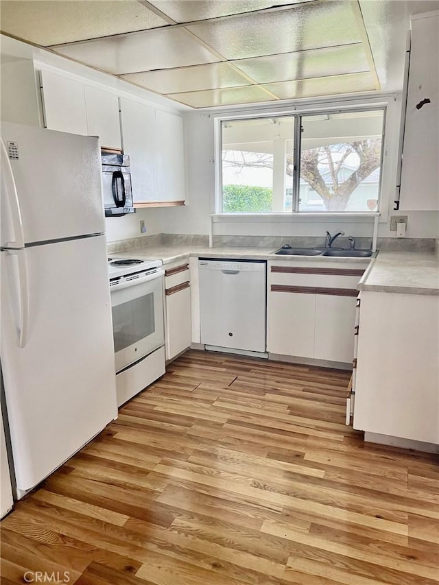 kitchen featuring white cabinets, white appliances, light countertops, and a sink