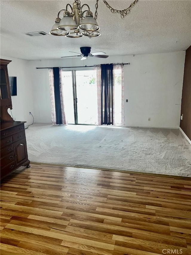 spare room featuring wood-type flooring, ceiling fan with notable chandelier, and a textured ceiling