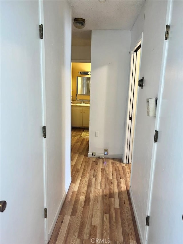 hall with a textured ceiling and light hardwood / wood-style flooring