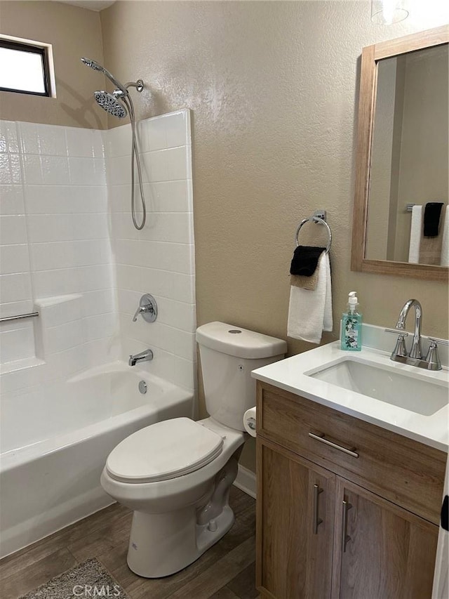 full bath with a textured wall, toilet, washtub / shower combination, vanity, and wood finished floors