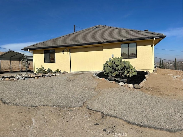 view of side of property with driveway, an attached garage, a tile roof, and stucco siding