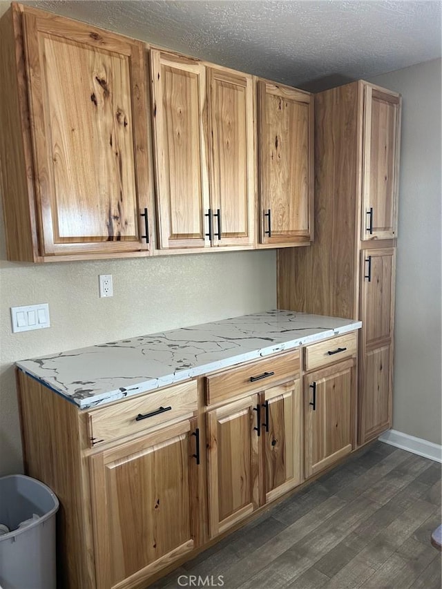 kitchen with light stone counters, dark wood finished floors, a textured ceiling, and baseboards