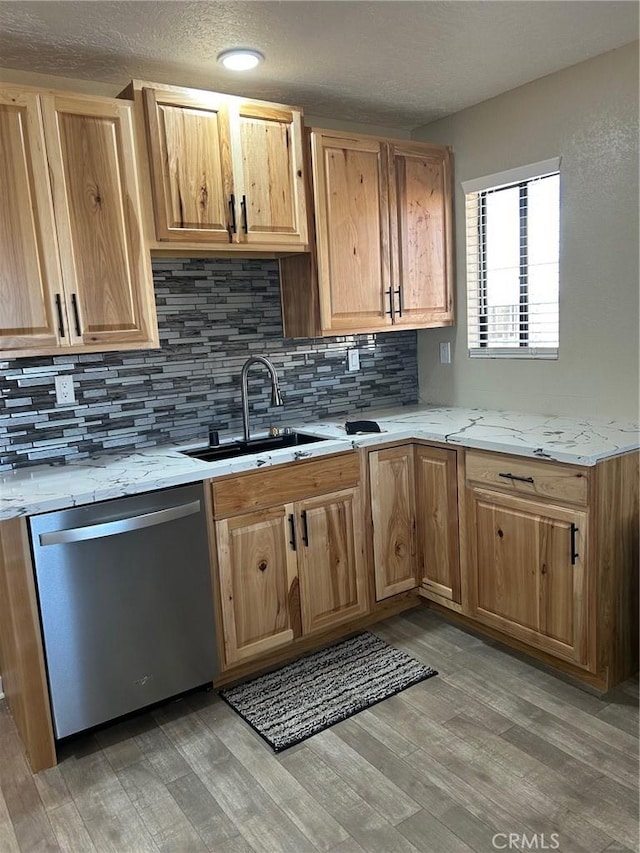 kitchen featuring light wood-style flooring, light stone counters, backsplash, stainless steel dishwasher, and a sink