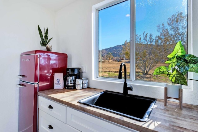 kitchen with butcher block countertops, white cabinetry, sink, a mountain view, and light wood-type flooring