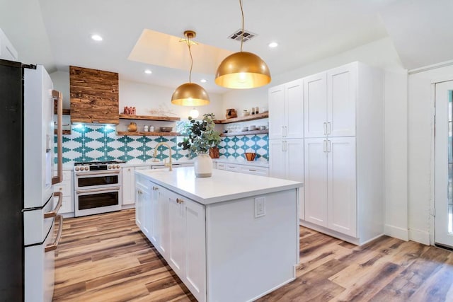 kitchen with white refrigerator, double oven range, decorative light fixtures, and white cabinets