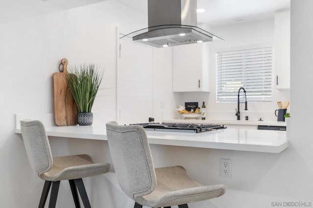 kitchen featuring built in desk, island range hood, stainless steel gas stovetop, white cabinetry, and sink