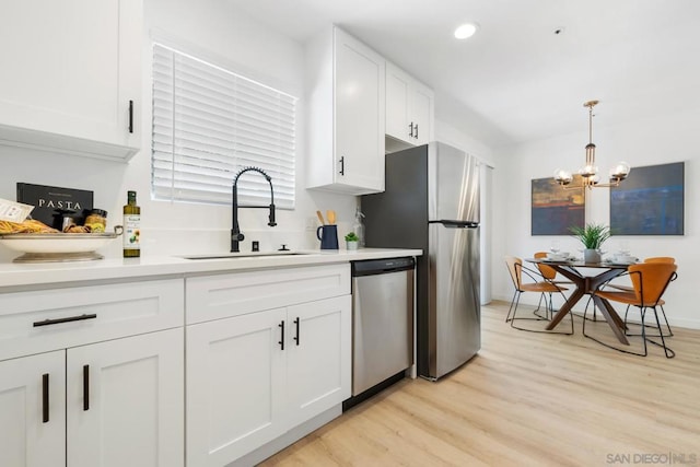 kitchen featuring pendant lighting, sink, stainless steel appliances, light hardwood / wood-style floors, and white cabinets