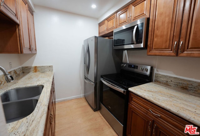 kitchen featuring light stone counters, appliances with stainless steel finishes, light hardwood / wood-style floors, and sink