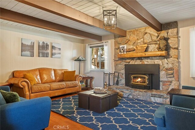 living room featuring wooden walls, a stone fireplace, wood finished floors, and beamed ceiling