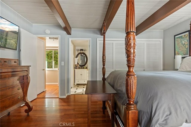 bedroom with two closets, wood finished floors, and beam ceiling