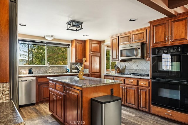 kitchen with appliances with stainless steel finishes, dark stone counters, dark wood-type flooring, and a center island