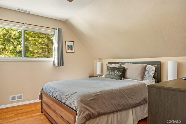 bedroom with light wood-type flooring, visible vents, lofted ceiling, and baseboards