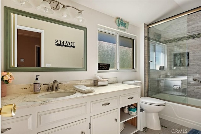 bathroom with bath / shower combo with glass door, wood finished floors, vanity, and toilet