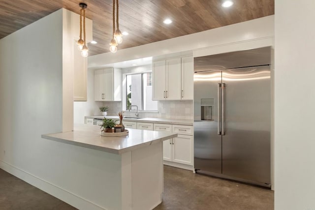 kitchen with tasteful backsplash, kitchen peninsula, built in fridge, pendant lighting, and white cabinets