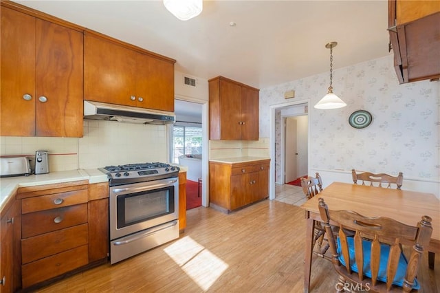 kitchen with gas range, hanging light fixtures, light hardwood / wood-style flooring, tile counters, and backsplash