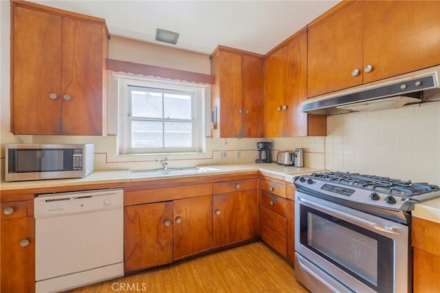 kitchen with stainless steel appliances, sink, backsplash, and light wood-type flooring