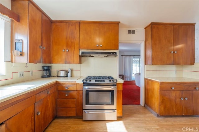 kitchen with tasteful backsplash, tile counters, light hardwood / wood-style floors, and gas stove