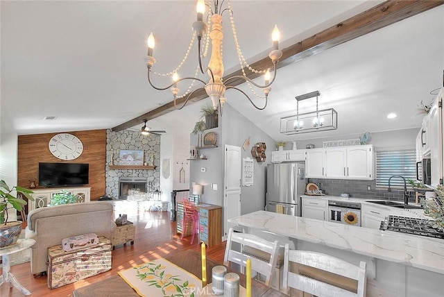 kitchen featuring sink, vaulted ceiling with beams, stainless steel appliances, light stone counters, and tasteful backsplash