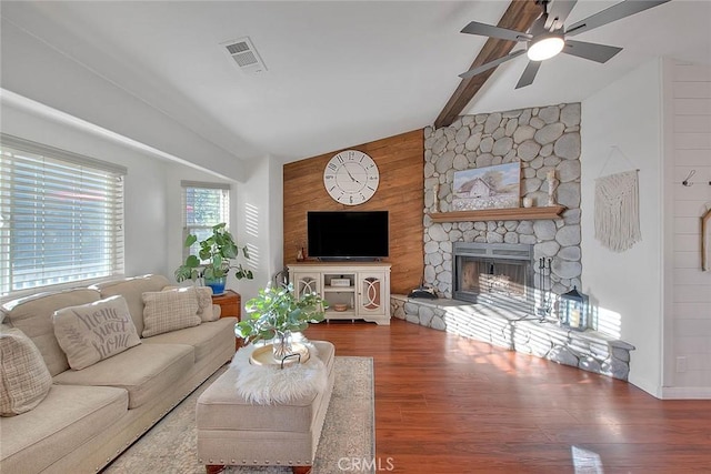 living room with a stone fireplace, wood walls, beamed ceiling, hardwood / wood-style flooring, and ceiling fan