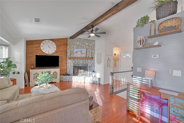 living room featuring ceiling fan, wood-type flooring, a fireplace, and vaulted ceiling with beams