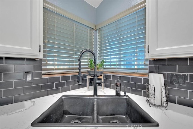 details with white cabinetry, sink, light stone counters, and backsplash