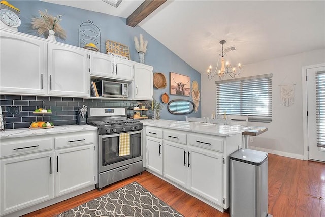 kitchen featuring appliances with stainless steel finishes, pendant lighting, lofted ceiling with beams, white cabinetry, and light stone countertops