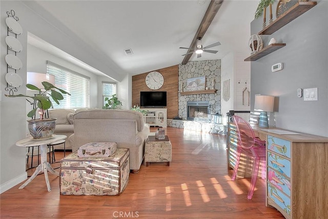 living room with a stone fireplace, wood-type flooring, lofted ceiling with beams, and ceiling fan