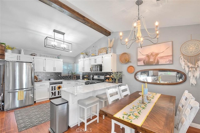 kitchen with sink, appliances with stainless steel finishes, white cabinets, decorative light fixtures, and kitchen peninsula