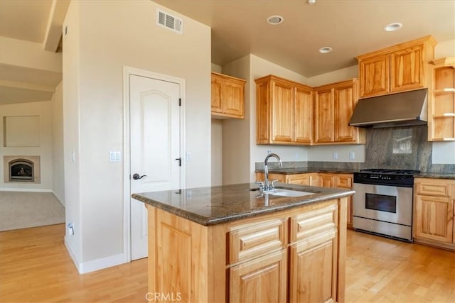 kitchen with sink, a kitchen island with sink, dark stone countertops, stainless steel range, and light wood-type flooring