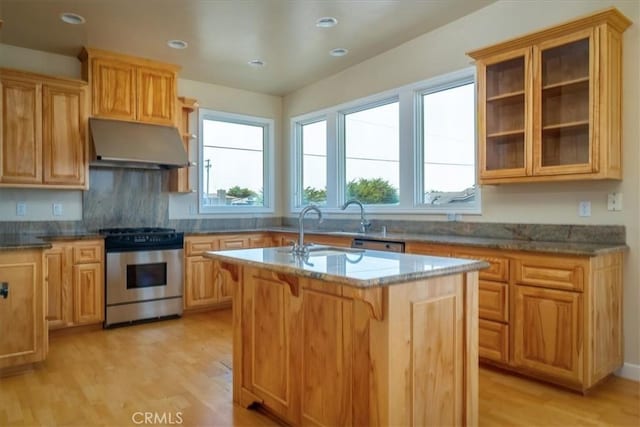 kitchen featuring stainless steel gas range oven, a kitchen island with sink, sink, and light hardwood / wood-style flooring