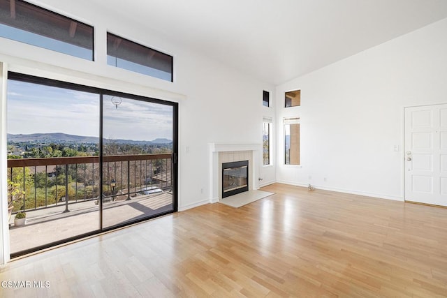 unfurnished living room featuring a tiled fireplace, a mountain view, a wealth of natural light, and light wood-type flooring