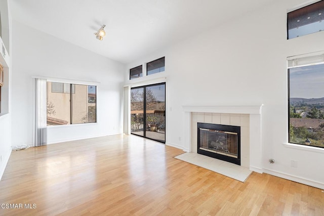 unfurnished living room with high vaulted ceiling, light hardwood / wood-style floors, and a tile fireplace