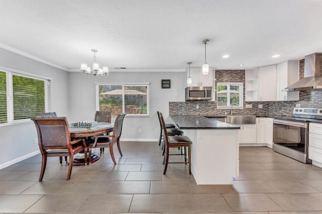 kitchen with pendant lighting, a kitchen breakfast bar, wall chimney exhaust hood, and appliances with stainless steel finishes