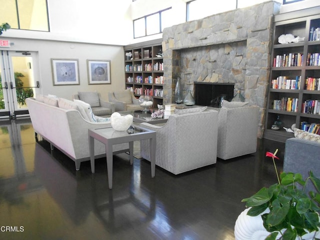 living room featuring a towering ceiling, a stone fireplace, dark wood-type flooring, and built in shelves