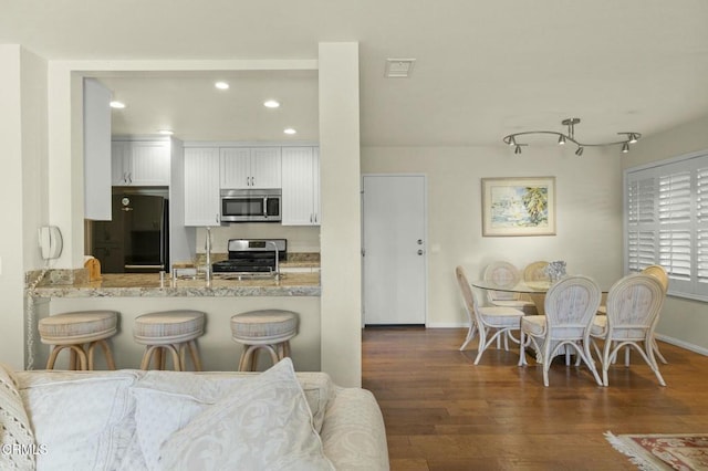 kitchen featuring dark hardwood / wood-style floors, white cabinetry, kitchen peninsula, stainless steel appliances, and light stone countertops