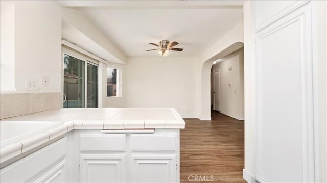 kitchen with hardwood / wood-style flooring, ceiling fan, white cabinetry, tile counters, and kitchen peninsula