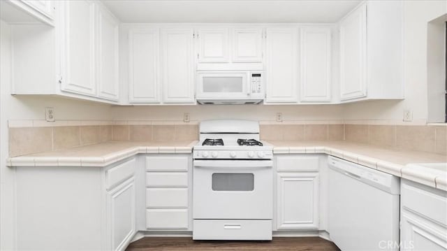 kitchen with dark wood-type flooring, white appliances, tile counters, and white cabinets