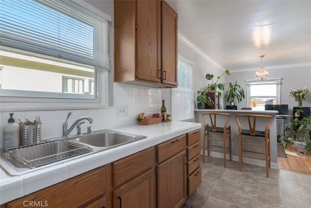 kitchen featuring decorative light fixtures, sink, backsplash, ornamental molding, and tile counters