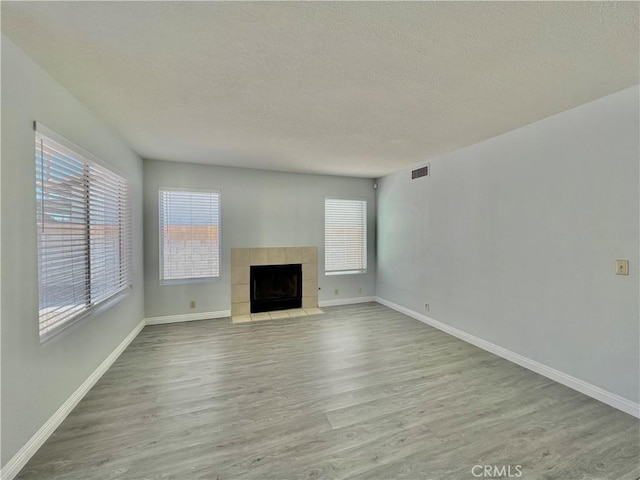 unfurnished living room with a tiled fireplace, light hardwood / wood-style flooring, and a textured ceiling