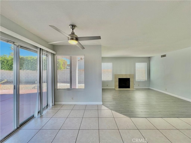 unfurnished living room featuring a tiled fireplace, a wealth of natural light, light tile patterned floors, and ceiling fan