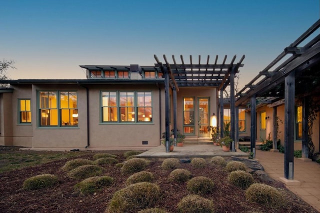 back house at dusk featuring a pergola and a patio