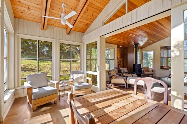 sunroom / solarium featuring vaulted ceiling with beams, ceiling fan, wooden ceiling, and a wood stove